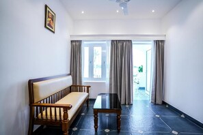 Ein Zimmer mit einer Couch, einem Tisch und Blick durch ein mit Vorhängen drapiertes Fenster.