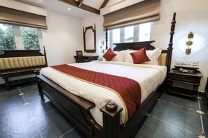 A bedroom with a large bed, a bedside table, a nightstand, a mirror, and a window with blinds. - Le Mont Lagoon Home Stay (Kochi)