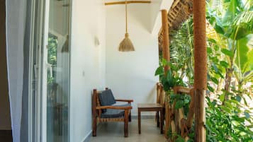 Quarto com porta de vidro deslizante, uma cadeira de madeira com almofada, uma mesinha e luminária pendente.