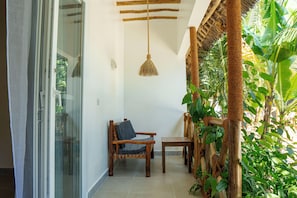 Quarto com porta de vidro deslizante, uma cadeira de madeira com almofada, uma mesinha e luminária pendente.