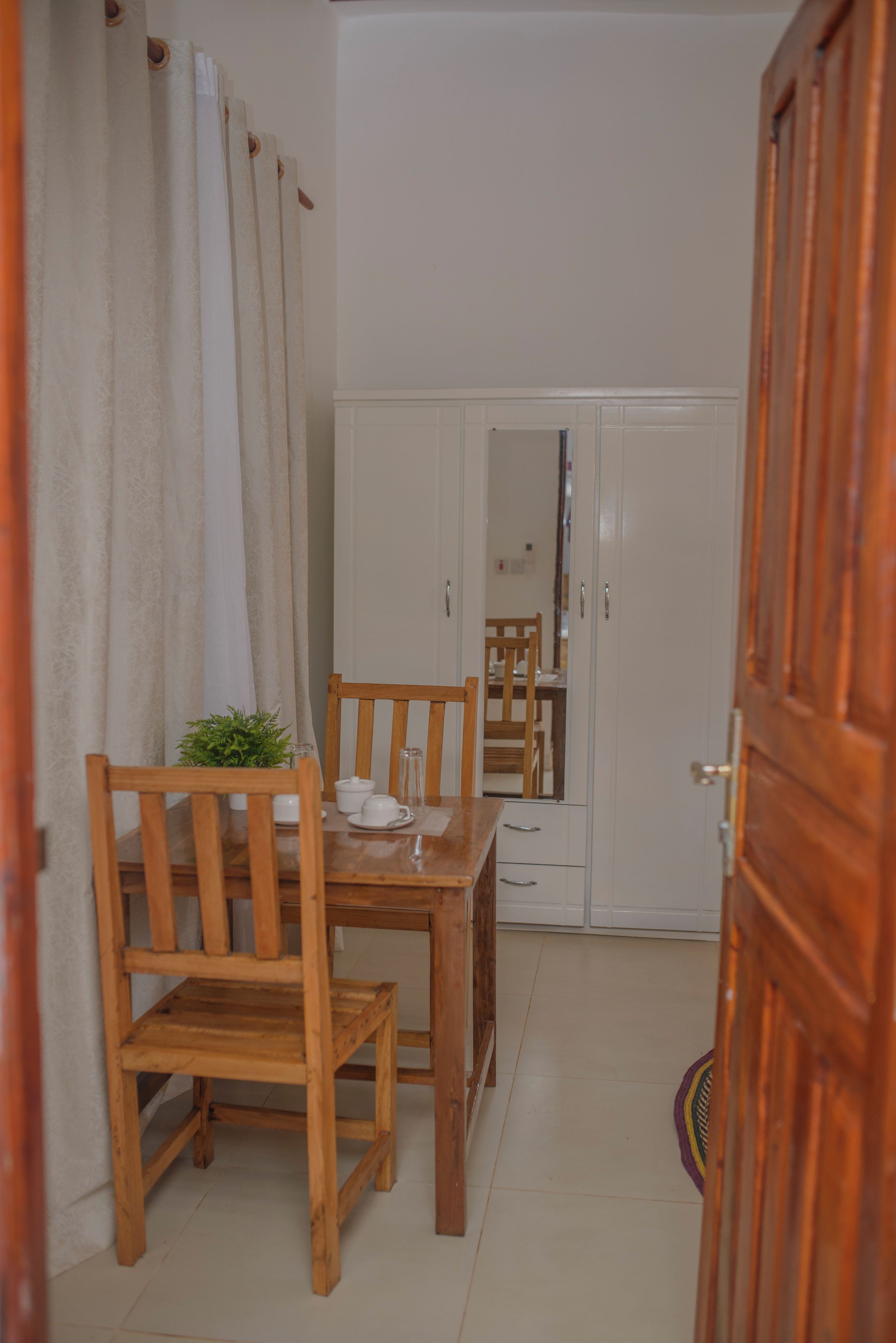 Una habitación con una mesa de comedor de madera y sillas, un armario blanco y un espejo en la pared.