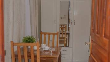 Una habitación con una mesa de comedor de madera y sillas, un armario blanco y un espejo en la pared.