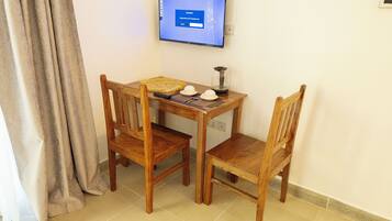 A small wooden table with two chairs, a television mounted on the wall, and a window with curtains.