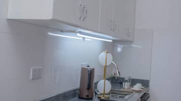 Een keuken met witte kasten, een gasfornuis, een koffiezetapparaat en een moderne lamp.