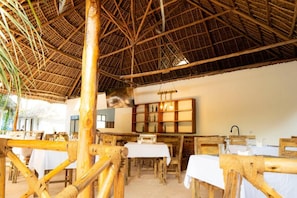 Un área de comedor al aire libre con mobiliario de madera y techo de paja.
