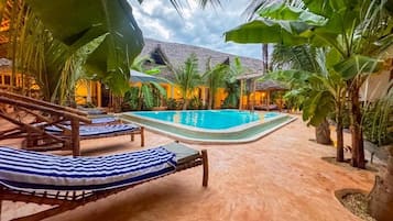 A pool area with lounge chairs and a thatched-roof structure.