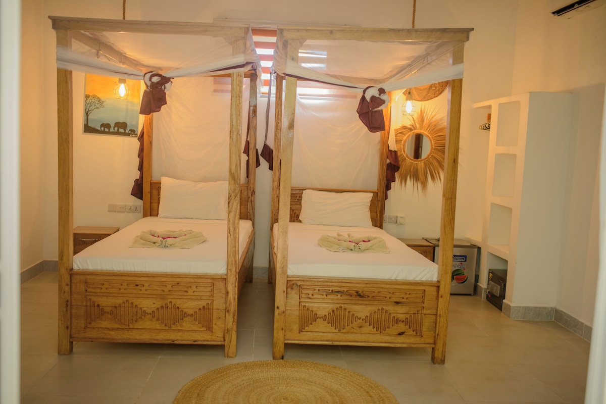 Quarto com duas camas de madeira, cada uma com dossel e uma mesinha de cabeceira.