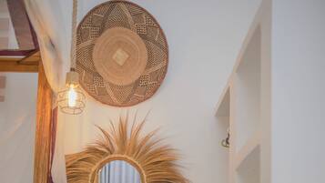 Un dormitorio con una cama, un aparador de madera, un refrigerador, un espejo montado en la pared y un espejo decorativo con forma de sol.