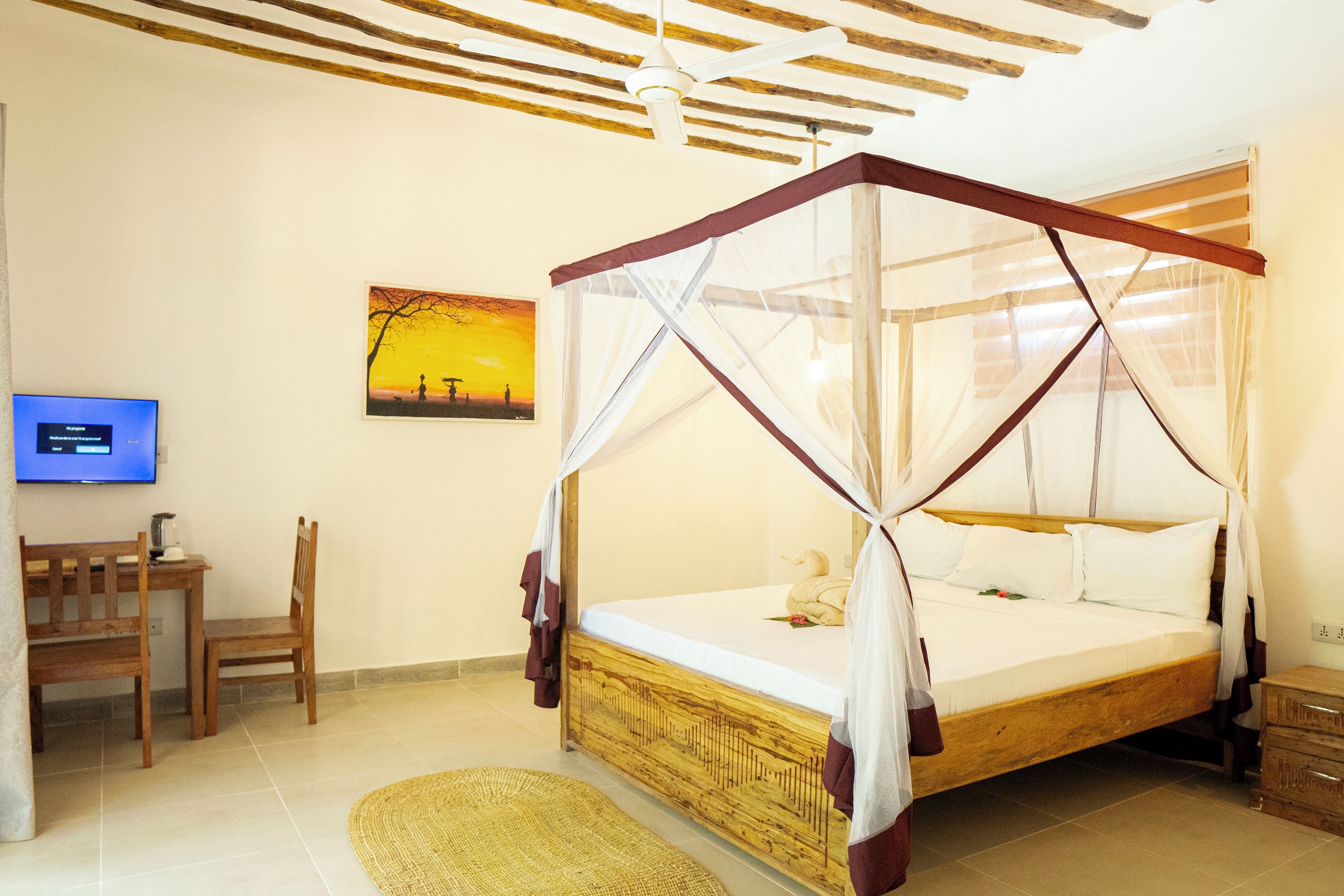 A bedroom with a four-poster bed, a television, a wooden chair, and a woven rug.