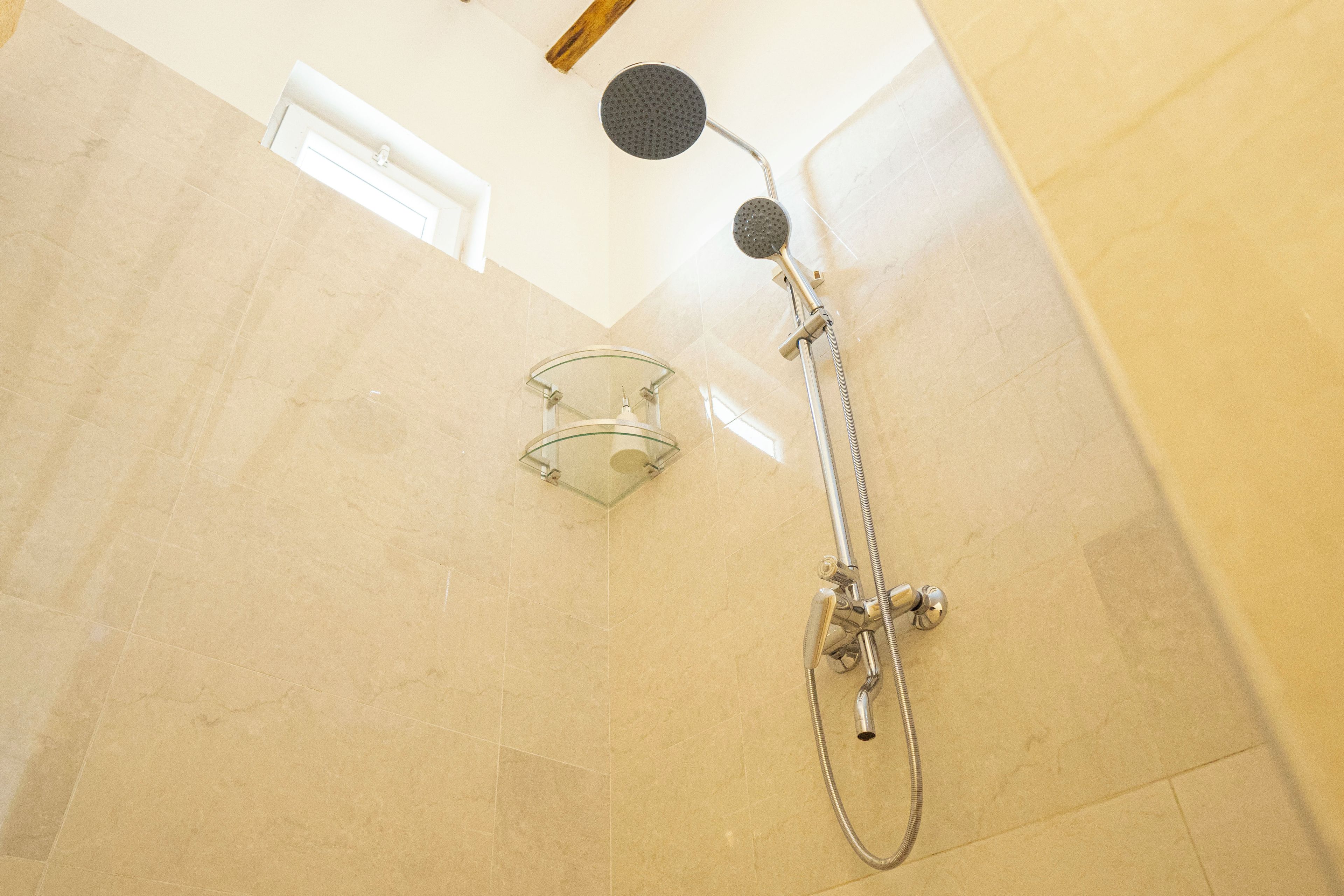 A shower with a glass-enclosed glass door, a handheld showerhead, and a wall-mounted faucet.
