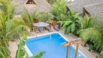 A swimming pool surrounded by palm trees and thatched-roof huts.