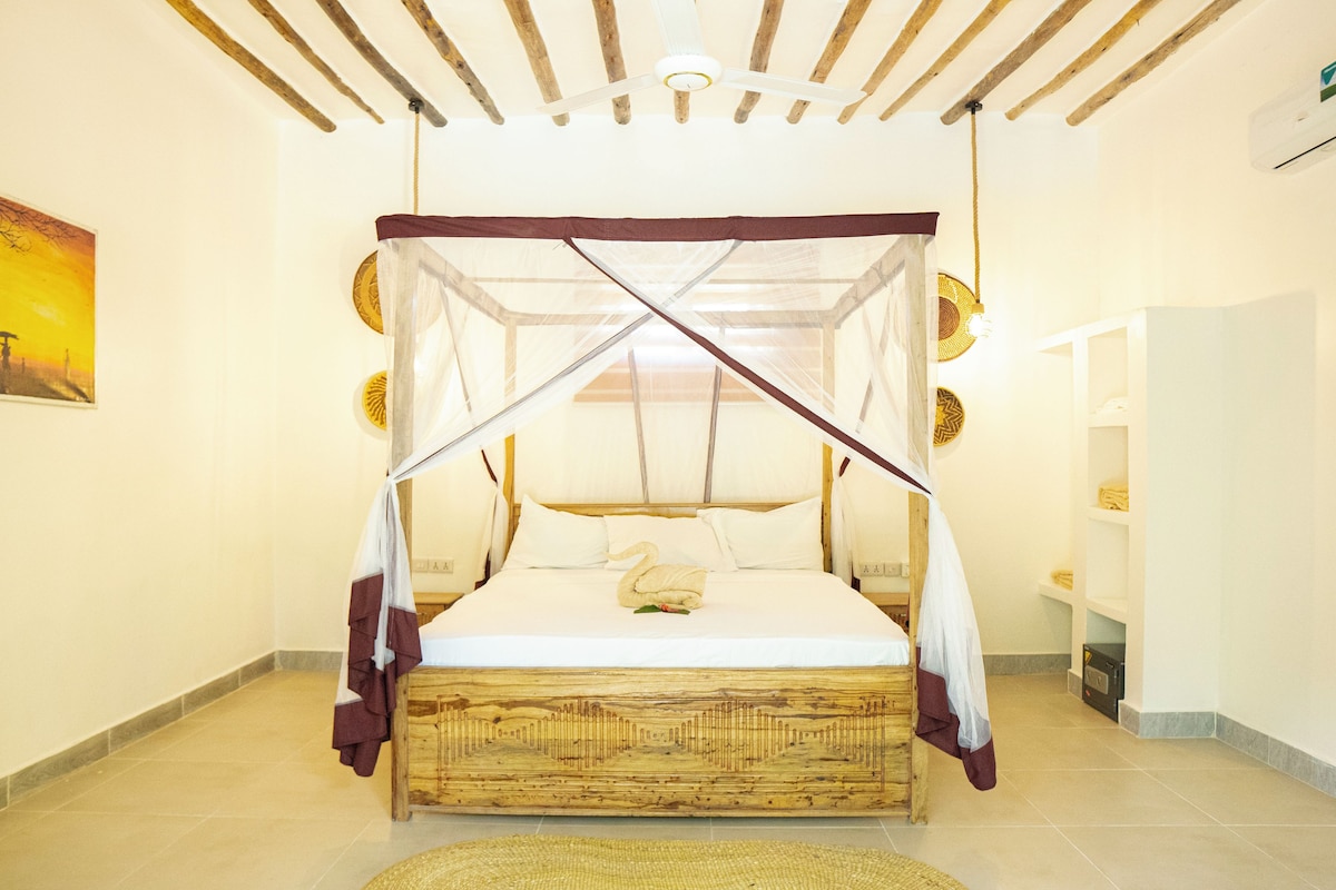 Una cama con dosel y pilares, cabecera de madera y almohada decorativa con forma de cisne.