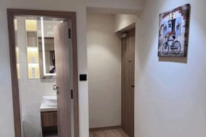 A hallway with a wooden door leading to a bathroom, a wooden wardrobe, and a wall-mounted painting of a bicycle. - Luxury Studio Apartment Khar West | Fully Furnished Mumbai Stay (Mumbai)