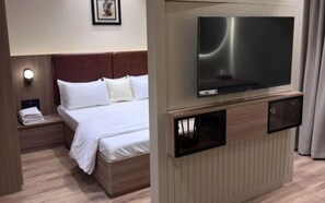 A hotel room with a bed, a TV mounted on a wooden cabinet, a nightstand with a lamp, and a framed picture on the wall. - Luxury Studio Apartment Khar West | Fully Furnished Mumbai Stay (Mumbai)