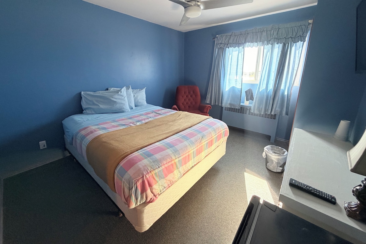 Een slaapkamer met een bed, een rode fauteuil, een plafondventilator en een raam met gordijnen.