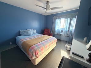 Een slaapkamer met een bed, een rode fauteuil, een plafondventilator en een raam met gordijnen.