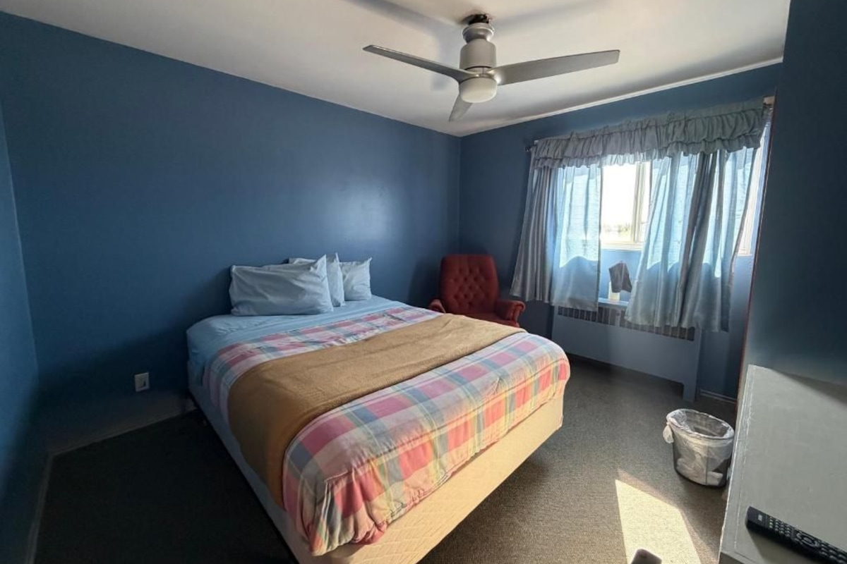 Un dormitorio con una cama, un ventilador de techo, una ventana con cortinas y una silla roja.
