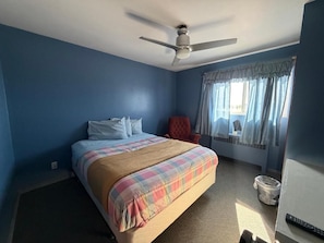 Un dormitorio con una cama, un ventilador de techo, una ventana con cortinas y una silla roja.