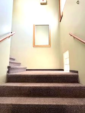 Una escalera con peldaños alfombrados, barandales y un cuadro en la pared.