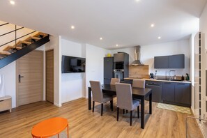 A modern kitchen with a dining area, a staircase, and a flat-screen TV. - The Nest of the Peaks (Formiguères)