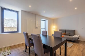 A modern living room with a dining table, chairs, a sofa, and a large window. - The Nest of the Peaks (Formiguères)