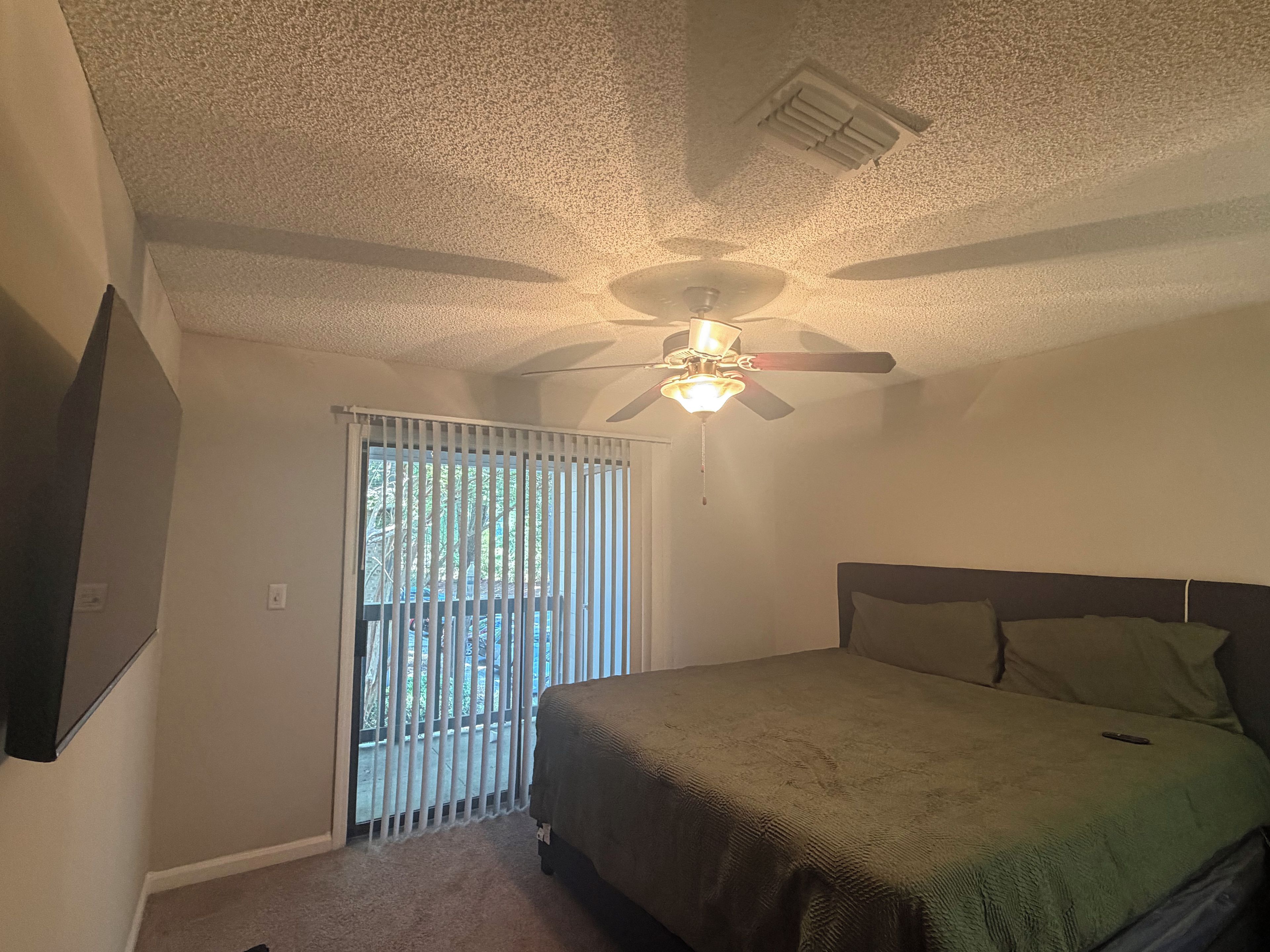 A bedroom with a bed, a ceiling fan, a window with blinds, and a door.