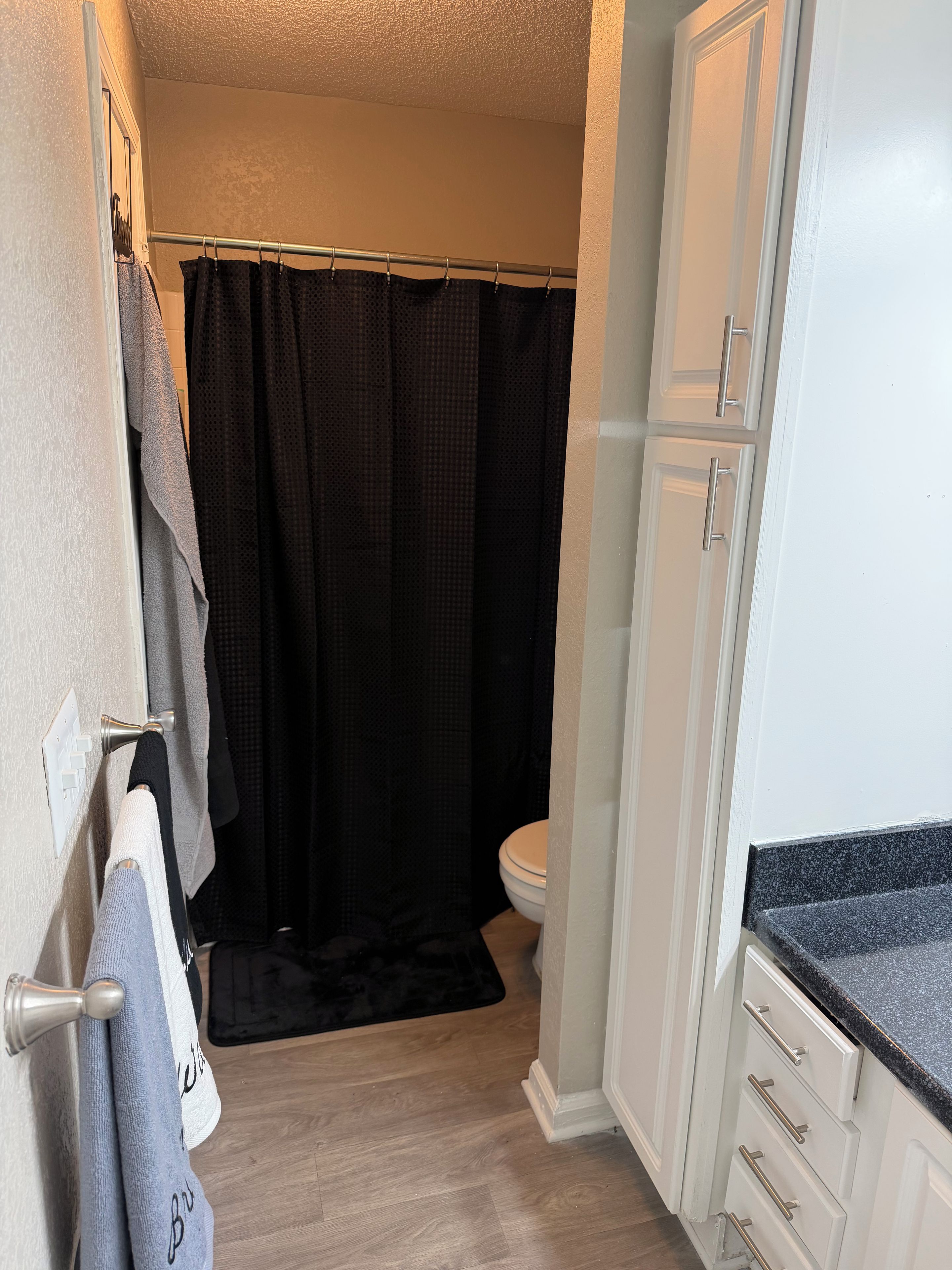Un baño con cortina de ducha, inodoro y toallero con toallas.