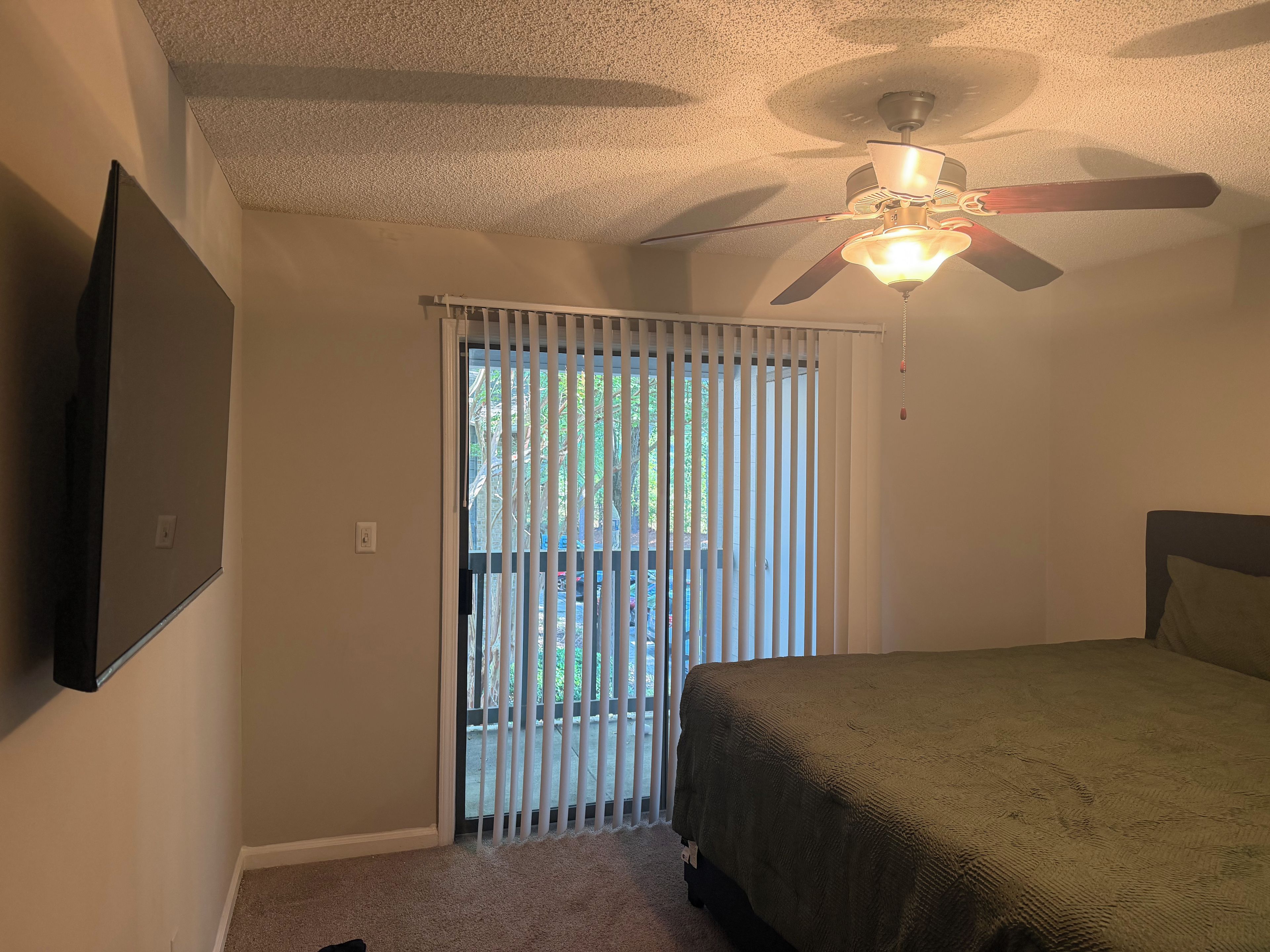 Quarto com cama, ventoinha no teto, janela com persianas e porta.