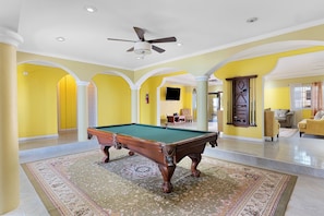 A spacious room with a pool table, a ceiling fan, and a large window. - Hospitality Expert VSV 6BR Chef Pool (Montego Bay)