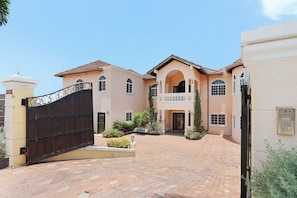 A large, two-story building with a gated entrance, multiple windows, and a paved driveway. - Hospitality Expert VSV 6BR Chef Pool (Montego Bay)