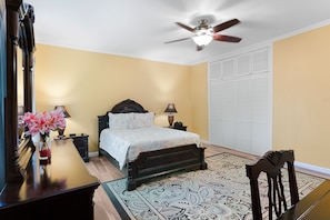 A bedroom with a bed, bedside tables, a desk, a chair, a ceiling fan, and a window with blinds. - Hospitality Expert VSV 6BR Chef Pool (Montego Bay)