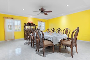 A dining room with a table set for six, surrounded by wooden chairs, in a room with yellow walls and a ceiling fan. - Hospitality Expert VSV 6BR Chef Pool (Montego Bay)