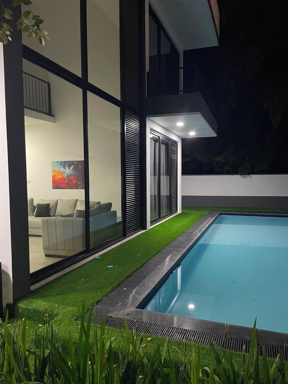 Una casa moderna con piscina, un ventanal que da a una sala de estar y una zona ajardinada.