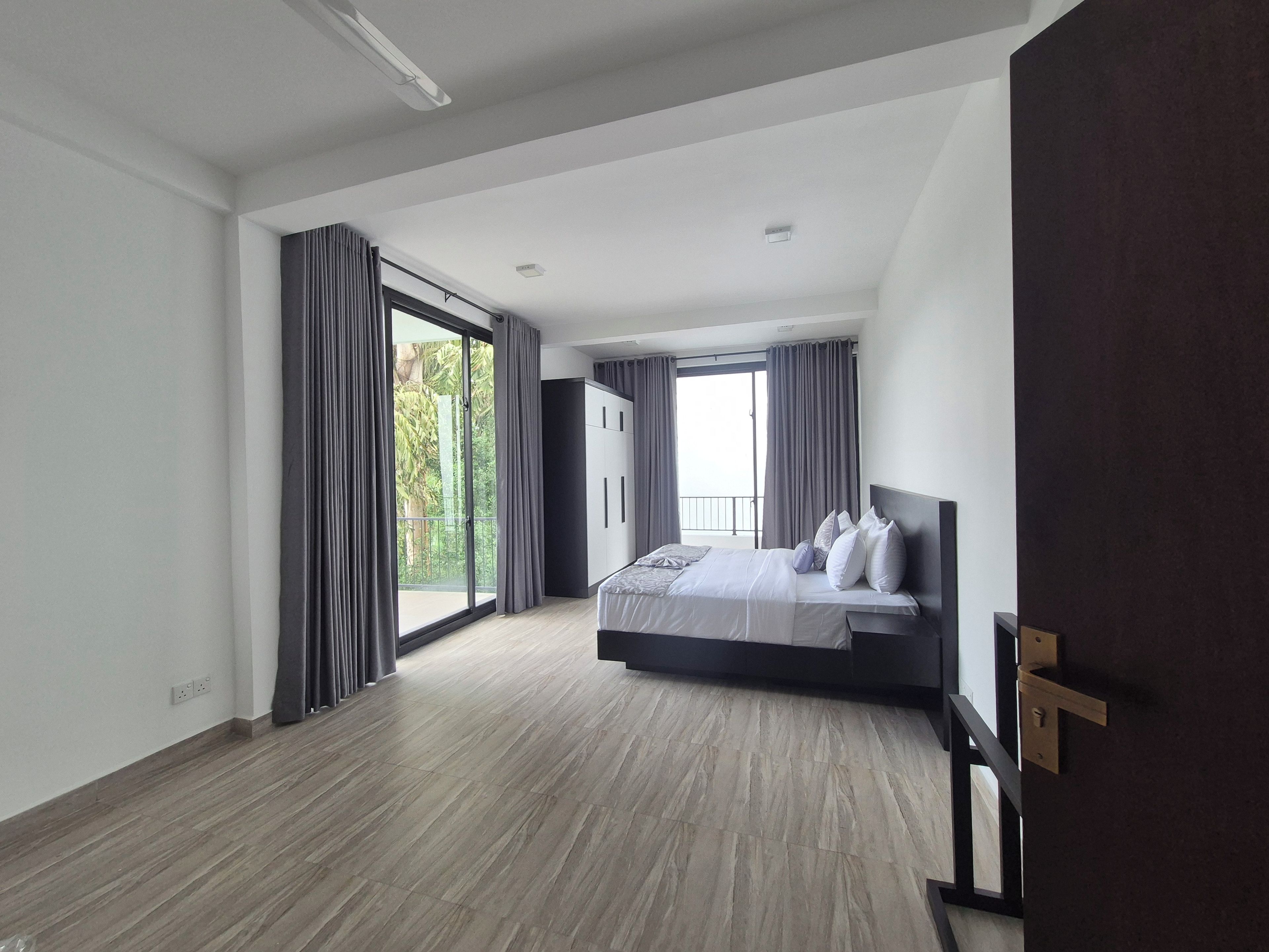 A modern bedroom with a large bed, a wardrobe, and a balcony with curtains.