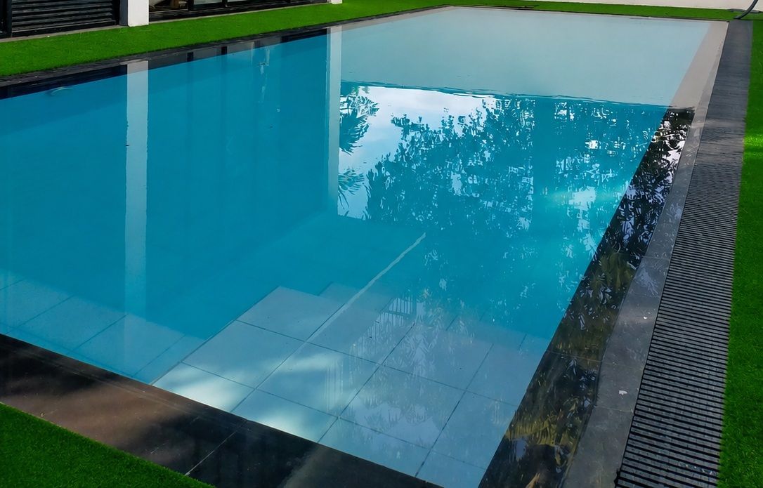 A swimming pool with clear water, surrounded by a tiled deck and a grassy area.
