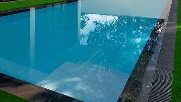 A swimming pool with clear water, surrounded by a tiled deck and a grassy area.