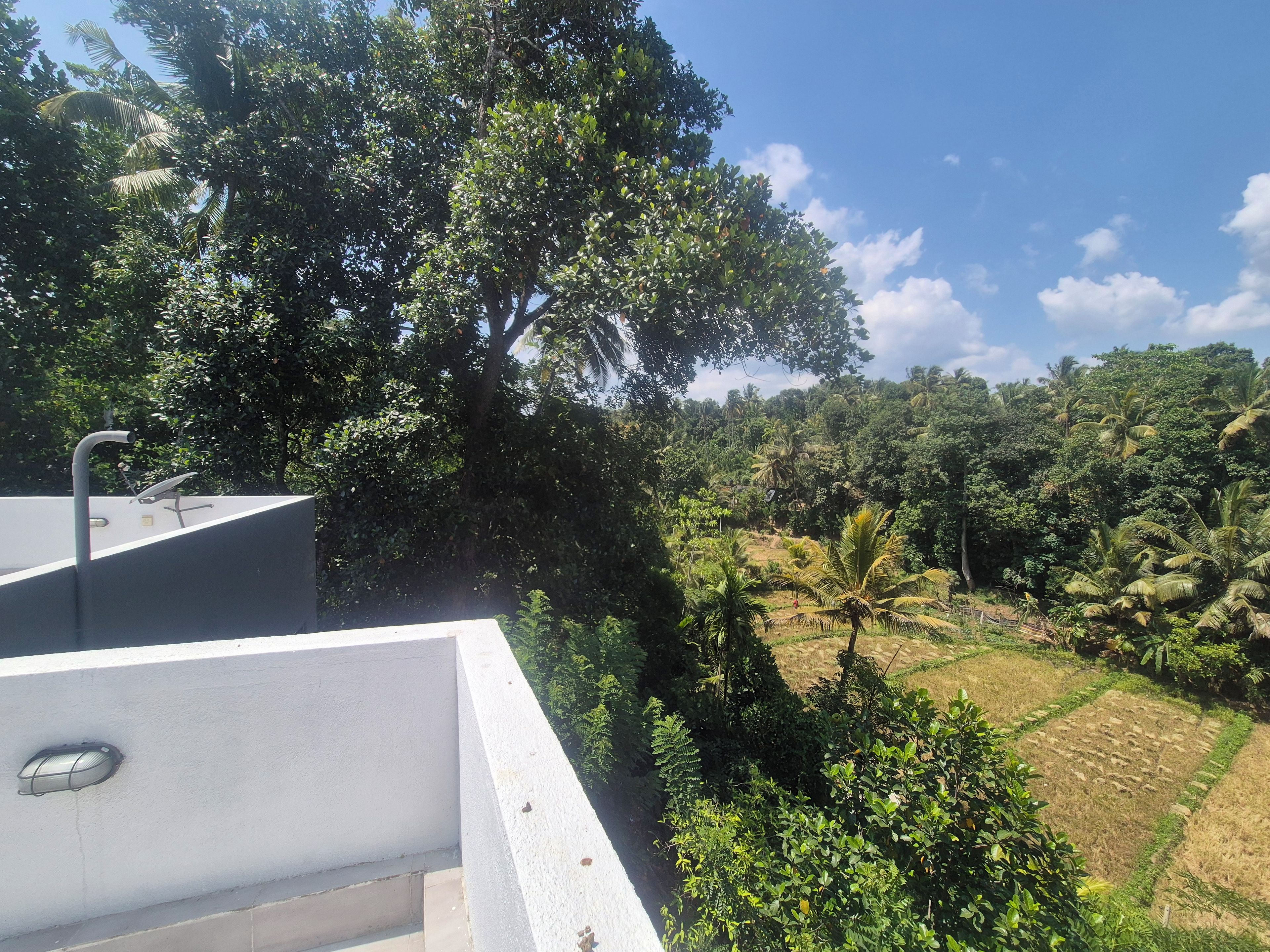 A rooftop with a white railing, a satellite dish, and a view of a lush green landscape with trees and a clear sky.