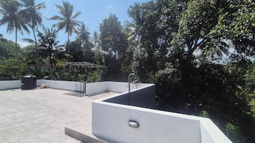 Een terras op het dak met een witte muur, een metalen hekwerk en een waterfontein.