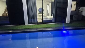 A modern pool area with a clear view of a bedroom through a glass door.