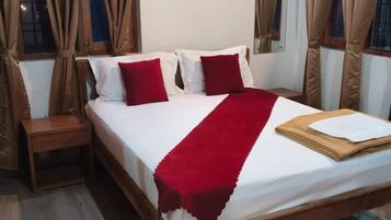 Een slaapkamer met een bed, kussens, een nachtkastje en gordijnen.