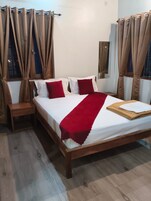Quarto com cama, almofadas, mesa de cabeceira e cortinas.