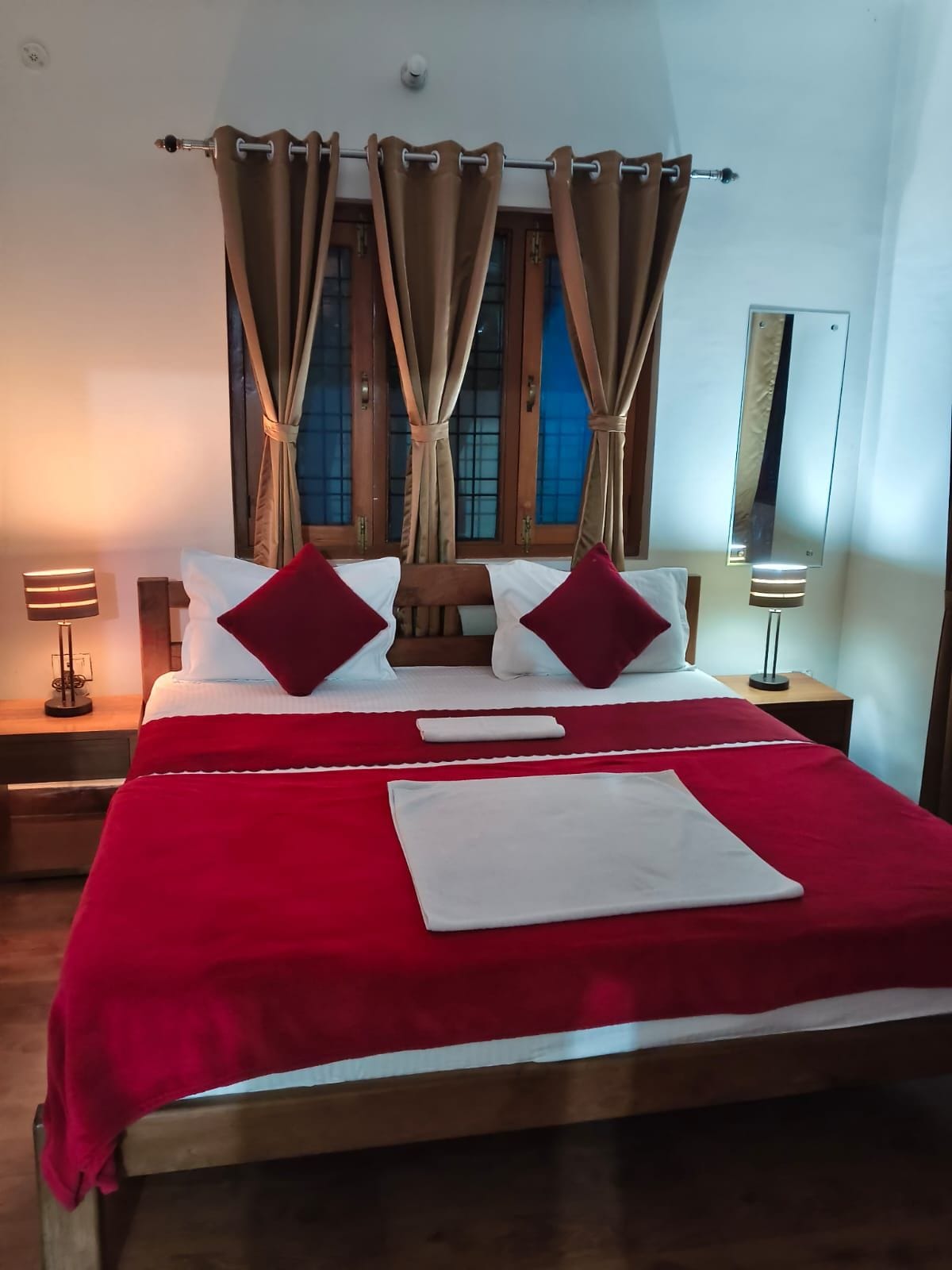 A neatly made bed with red and white bedding, a wooden headboard, and a window with curtains.