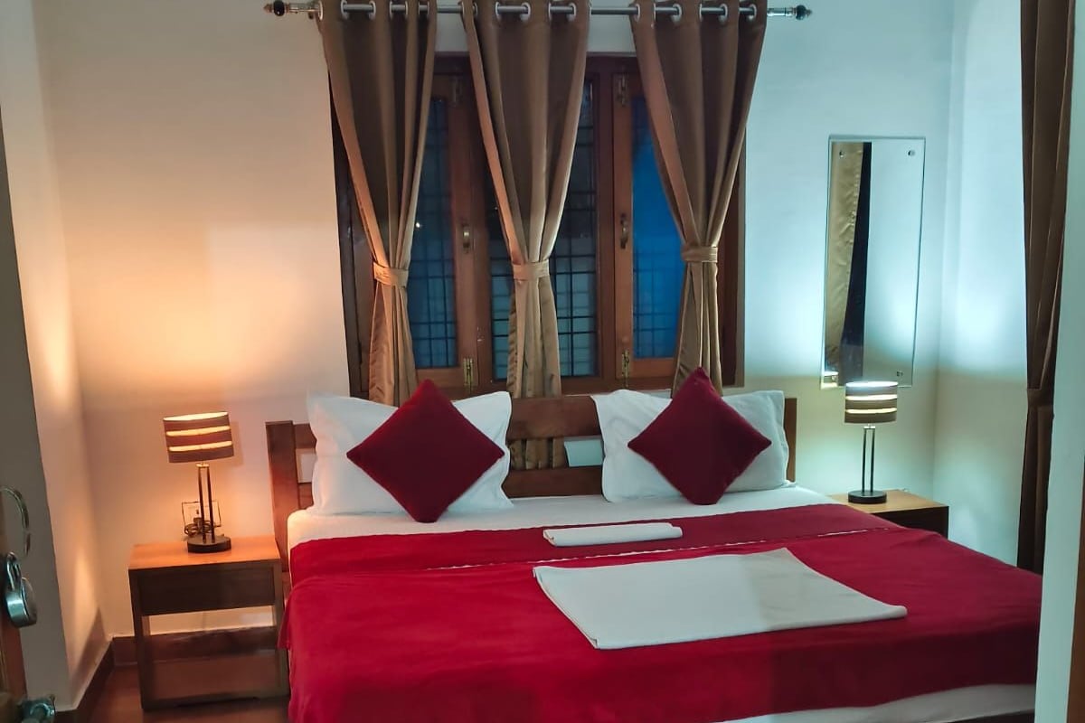 A bedroom with a wooden bed, red bedding, two bedside lamps, and a window with curtains.