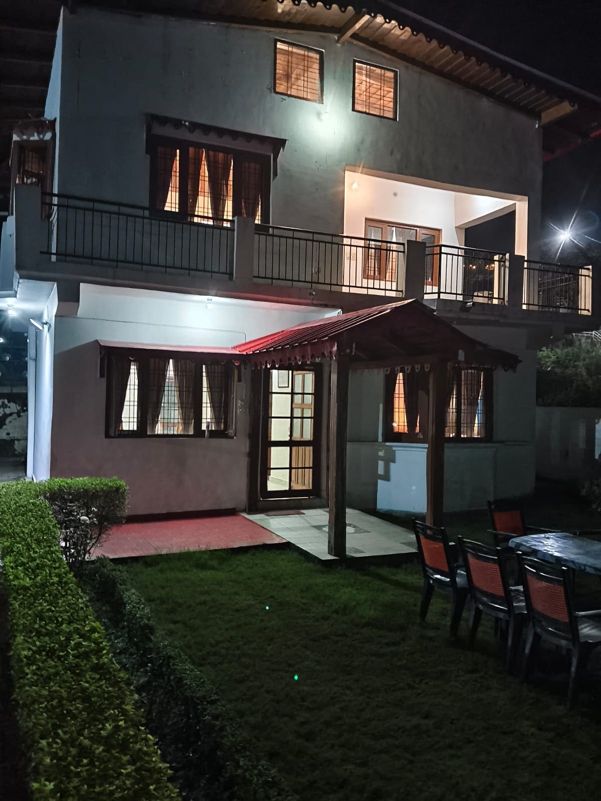 A two-story building with a balcony, a covered patio, and a lawn area with chairs.
