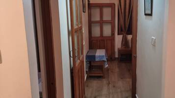 Een gang met een houten deur, een kleine tafel met tafelkleed en een wandlamp.
