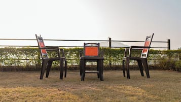 Three chairs with a mesh backrest and a central chair with a solid backrest, positioned on a grassy area with a metal railing in the background.
