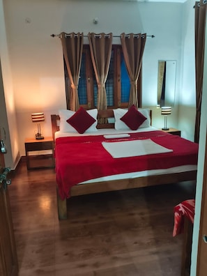 Quarto com cama de madeira, roupa de cama vermelha, duas luminárias de cabeceira e janela com cortinas.