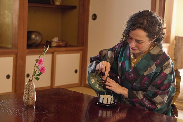 A person pouring tea from a teapot into a cup on a wooden table.