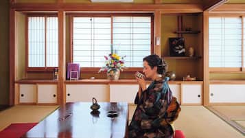 Ein traditioneller japanischer Raum mit Tatami-Böden, einem niedrigen Holztisch und einer Person, die auf einem roten Kissen sitzt.