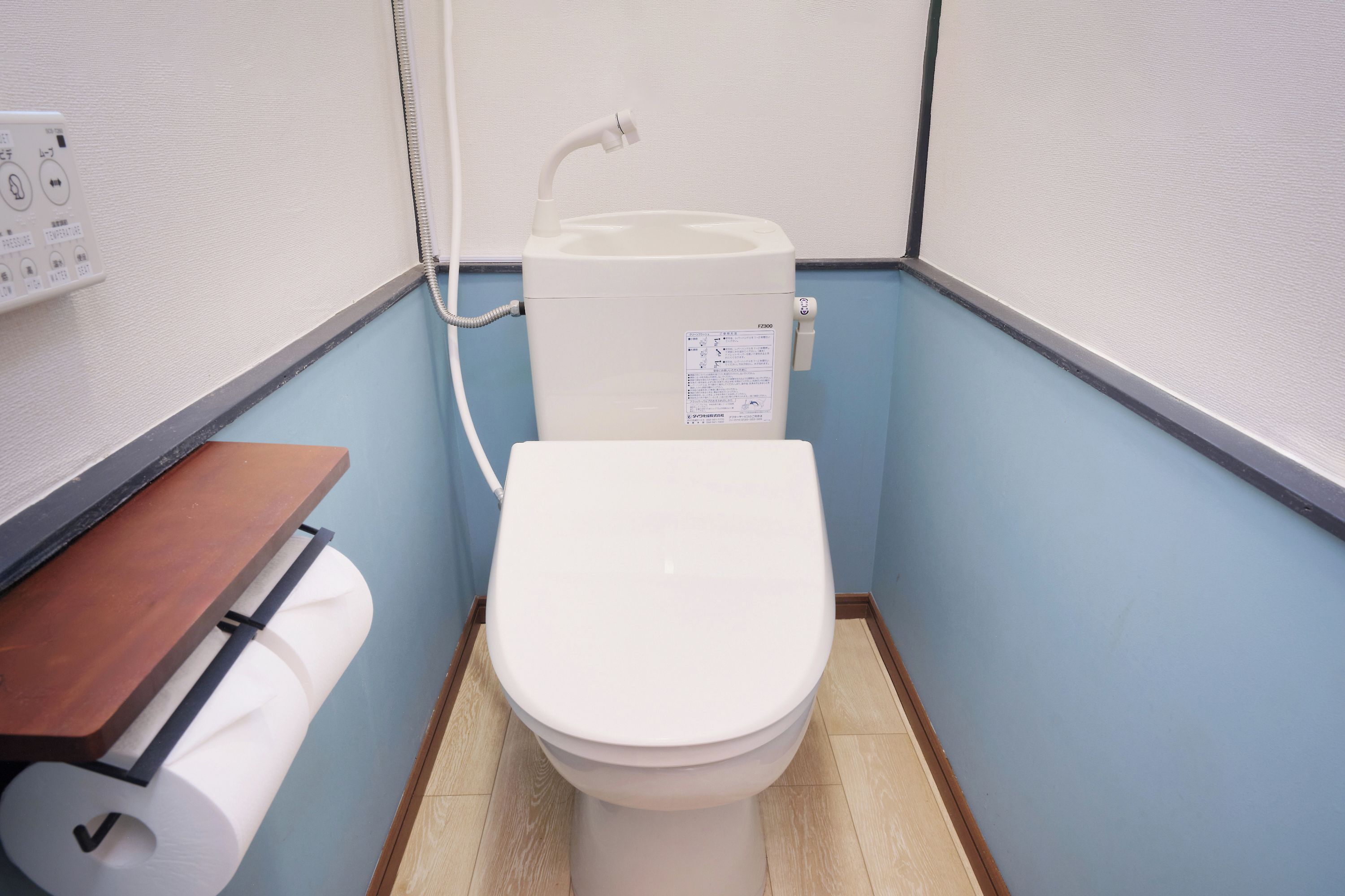 A small, compact bathroom with a toilet, a wooden shelf, and a roll of toilet paper.